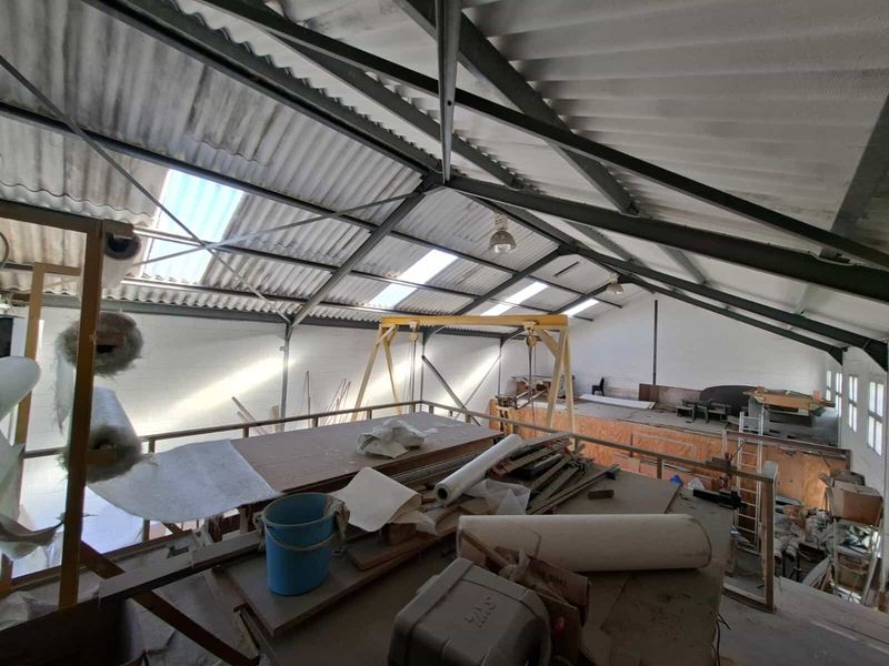 Spacious industrial utility area featuring exposed steel roof trusses, integrated skylights, and a built-in gantry crane system over a mezzanine level.