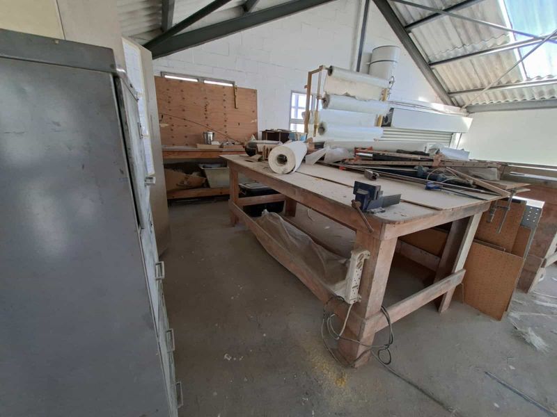 Industrial utility space featuring exposed steel roof trusses, corrugated metal roofing, and concrete flooring, suitable for workshop or storage use.