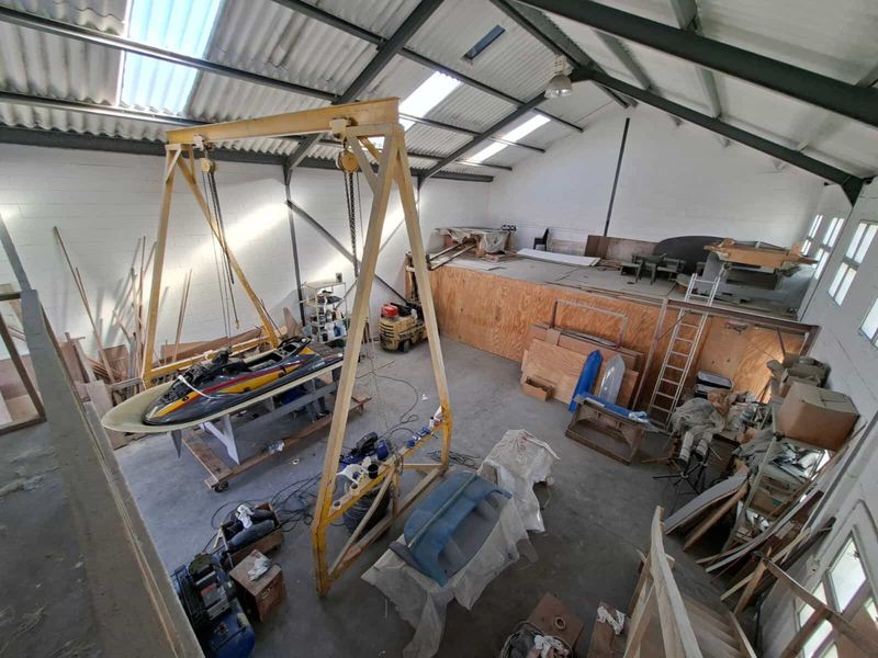 Spacious industrial workshop featuring high ceilings with exposed steel trusses, skylights, concrete flooring, and a mezzanine level suitable for various commercial or storage uses.