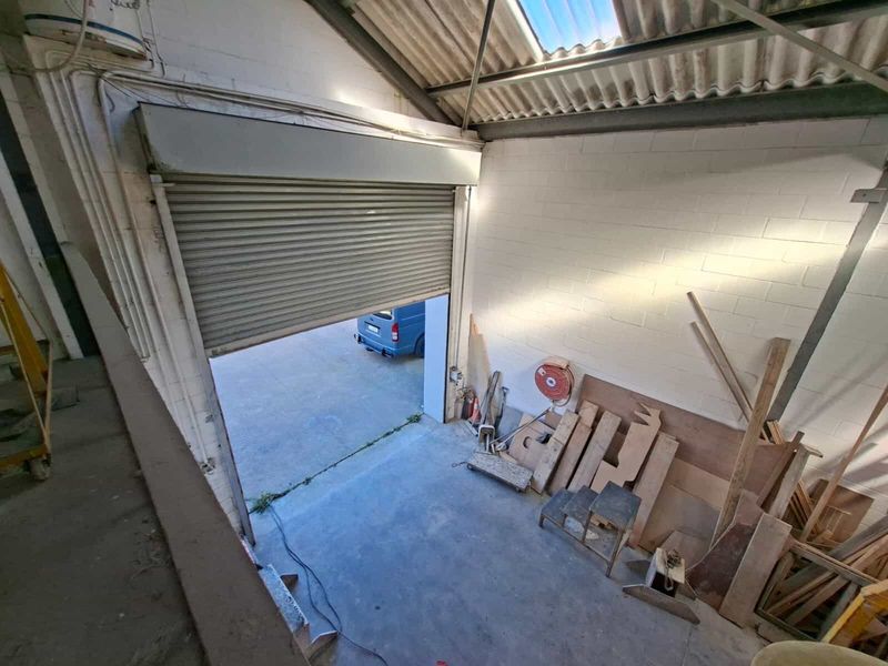 Industrial garage space featuring a large roller shutter door, exposed steel roof trusses, and durable concrete flooring, suitable for storage or workshop use.
