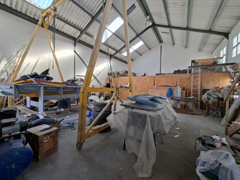 Spacious industrial workshop featuring high ceilings with exposed steel trusses, skylights, concrete flooring, and a built-in gantry crane for heavy lifting.