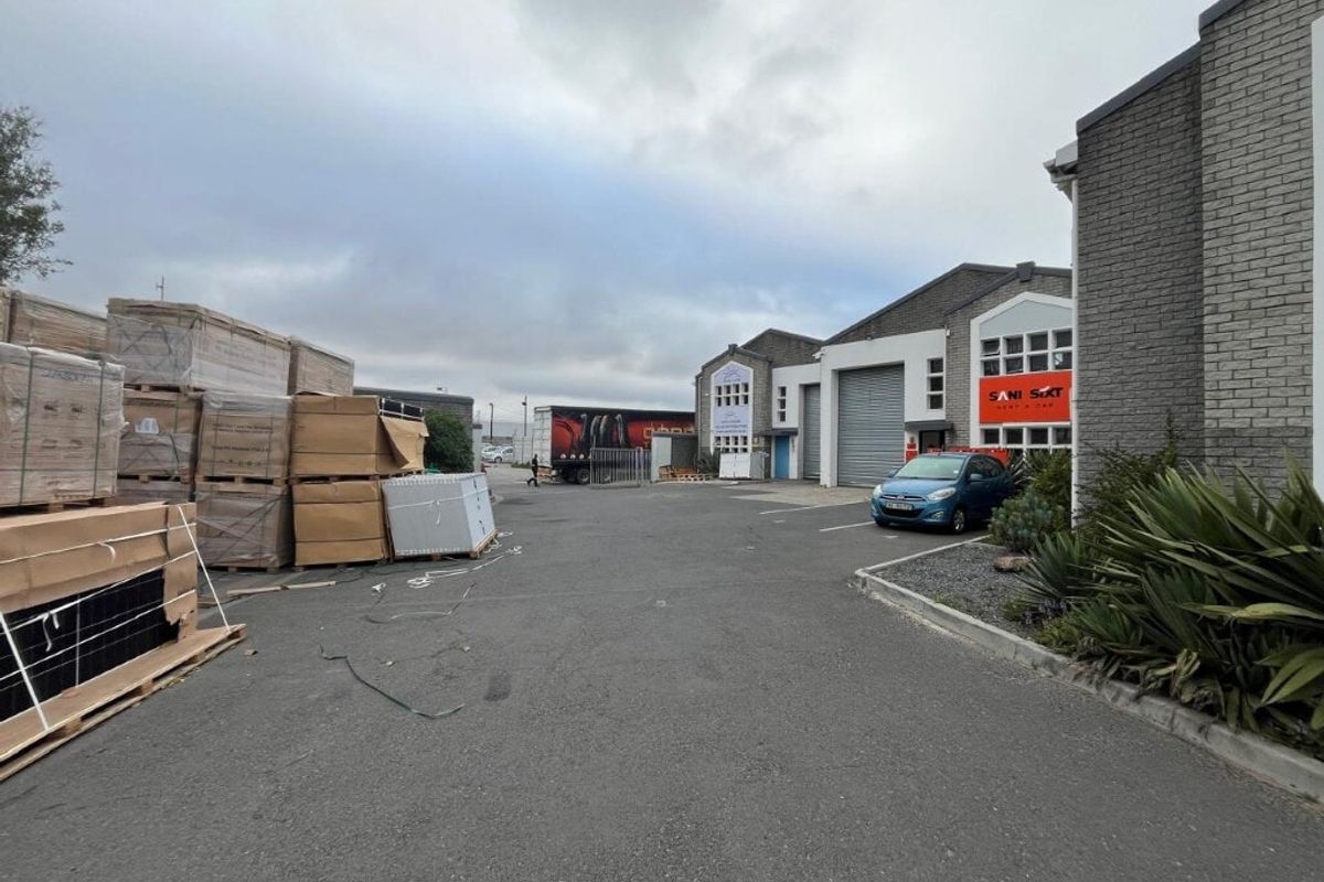 Industrial property exterior featuring a paved driveway, brick facade, and multiple roller shutter doors for commercial access.