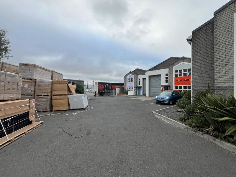 Industrial property exterior featuring a paved driveway, brick facade, and multiple roller shutter doors for commercial access.