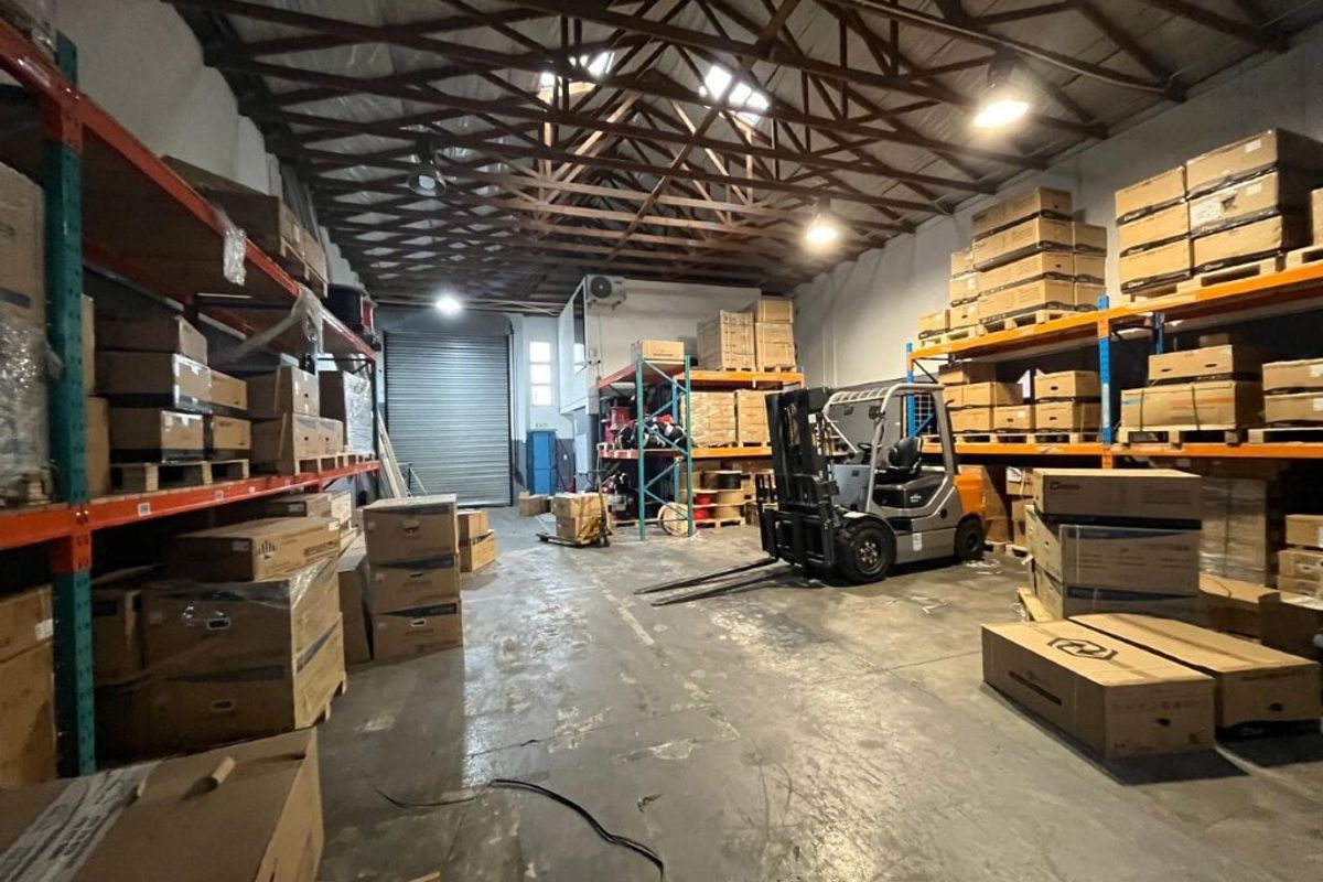 Spacious industrial warehouse unit featuring high-clearance timber roof trusses, concrete flooring, and integrated heavy-duty racking systems with a large roller shutter door.