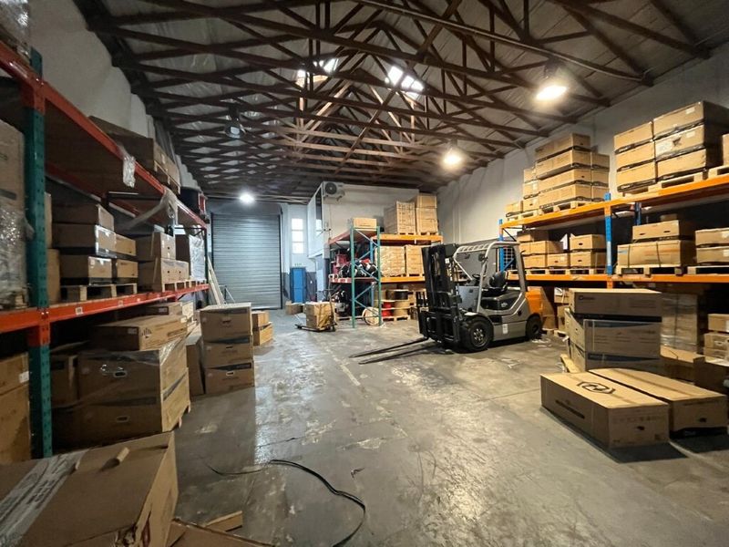 Spacious industrial warehouse unit featuring high-clearance timber roof trusses, concrete flooring, and integrated heavy-duty racking systems with a large roller shutter door.