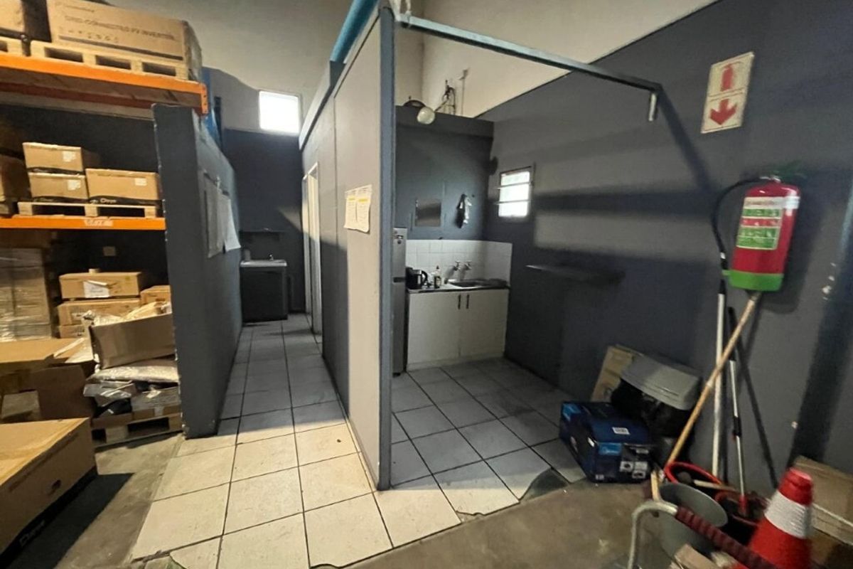 A functional kitchenette area within an industrial warehouse space, featuring basic cabinetry, a sink, and tiled flooring.
