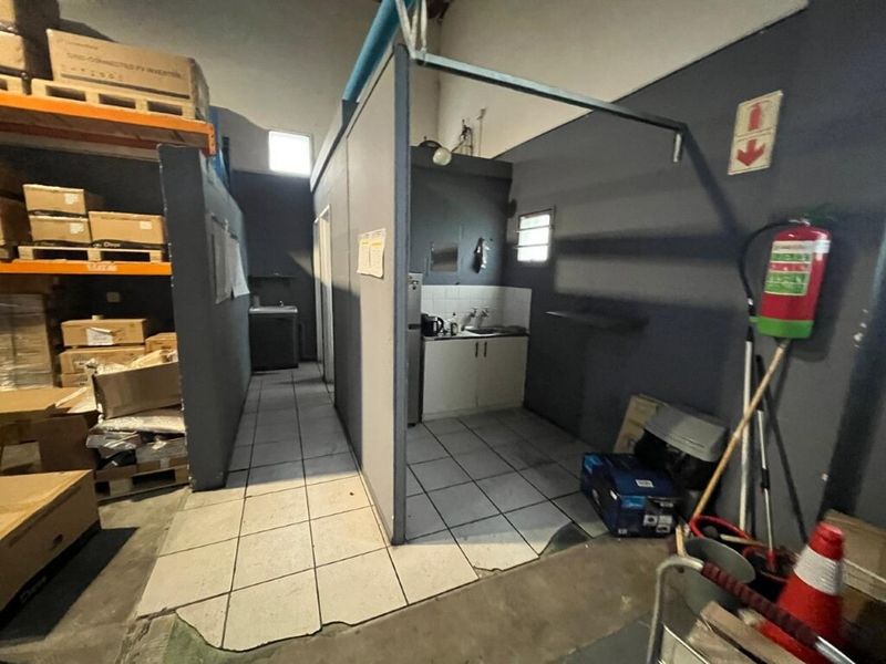 A functional kitchenette area within an industrial warehouse space, featuring basic cabinetry, a sink, and tiled flooring.