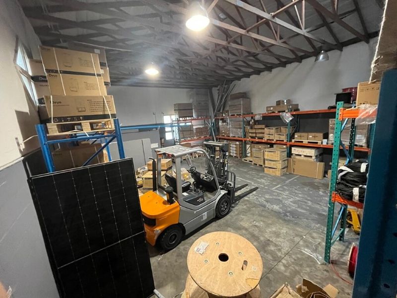 Industrial warehouse space featuring exposed steel roof trusses, concrete flooring, and extensive built-in racking systems for storage.