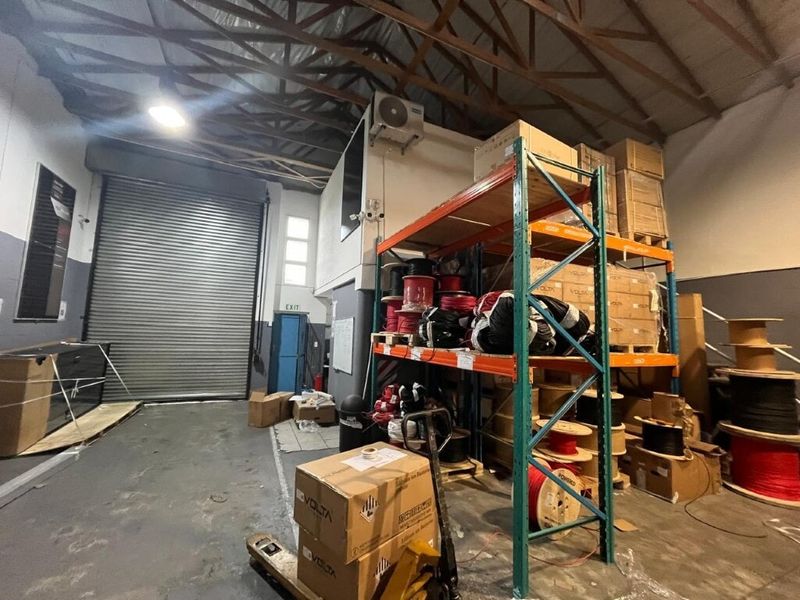 Industrial warehouse space featuring high ceilings with exposed trusses, a large roller shutter door, and heavy-duty storage racking.