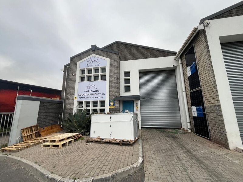 Front elevation of an industrial property featuring a roller shutter door, brick facade, and paved driveway access.