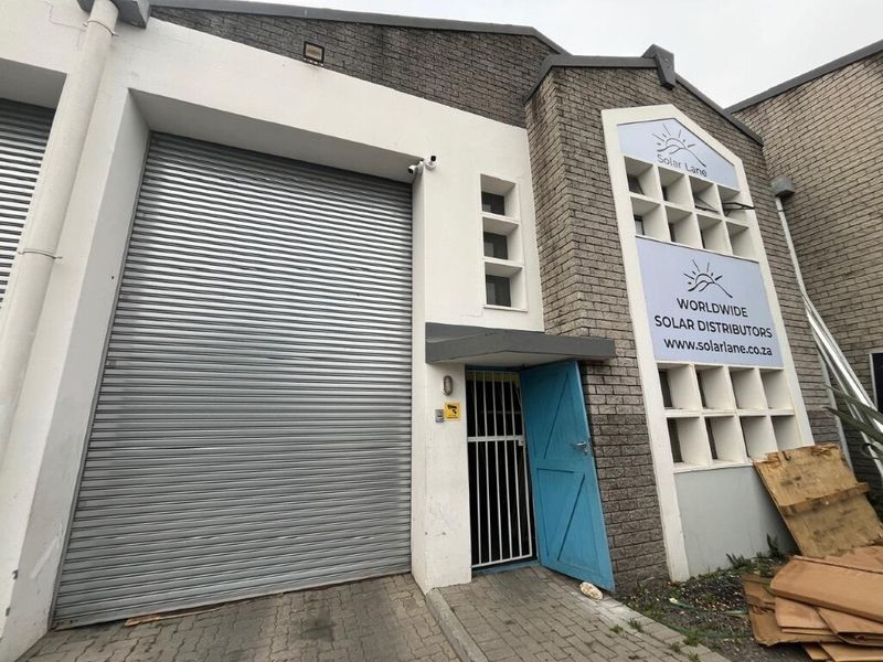 Industrial warehouse unit featuring a large roller shutter door, secure pedestrian entrance, and brick facade with prominent signage.