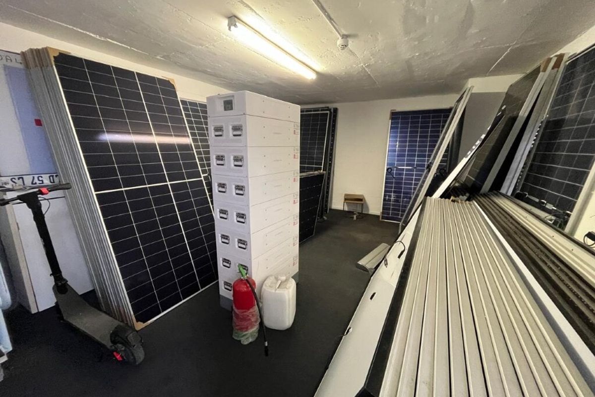 A utility storage area currently used for housing solar panels and equipment, featuring industrial lighting and concrete ceiling finishes.