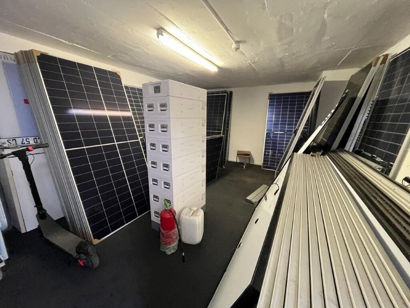 A utility storage area currently used for housing solar panels and equipment, featuring industrial lighting and concrete ceiling finishes.