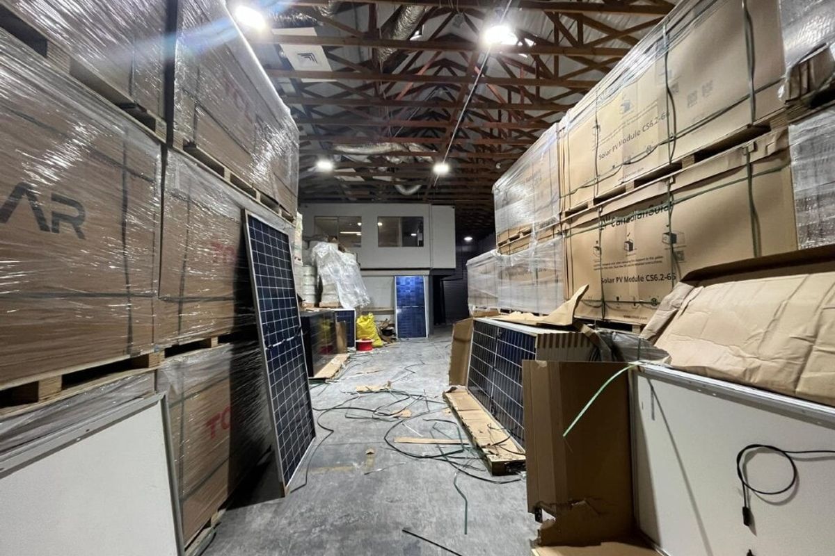 Industrial warehouse space featuring exposed timber roof trusses, concrete flooring, and a mezzanine office window, currently utilized for storage.