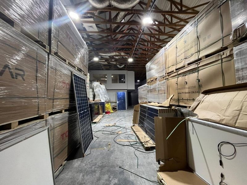 Industrial warehouse space featuring exposed timber roof trusses, concrete flooring, and a mezzanine office window, currently utilized for storage.