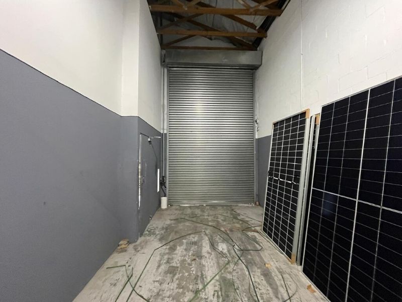 Industrial garage space featuring a large roller shutter door, exposed timber roof trusses, and durable concrete flooring.