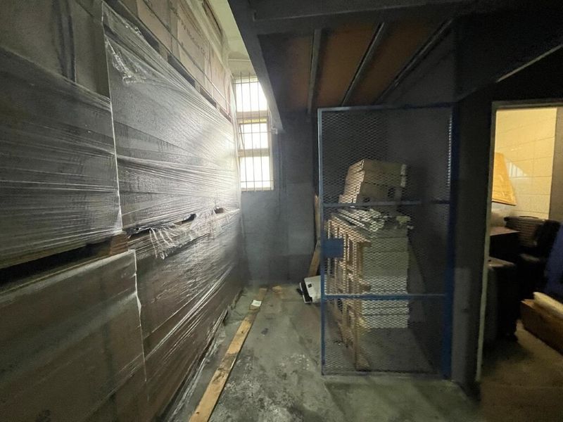 Industrial utility or storage area featuring a steel mezzanine structure, security gate, and reinforced window bars, suitable for warehouse or workshop use.