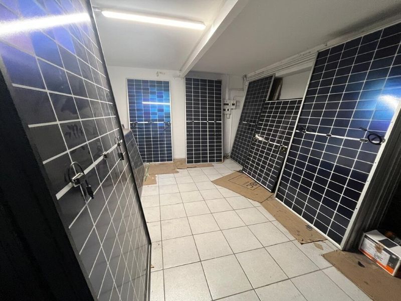 A functional utility space featuring tiled flooring, overhead fluorescent lighting, and an electrical distribution board, currently used for storage.