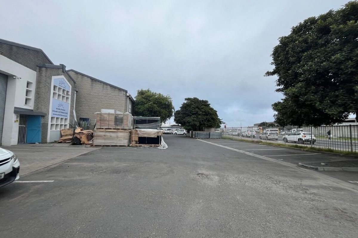 Exterior view of an industrial property featuring an asphalt driveway, security fencing, and access to the main building facade.