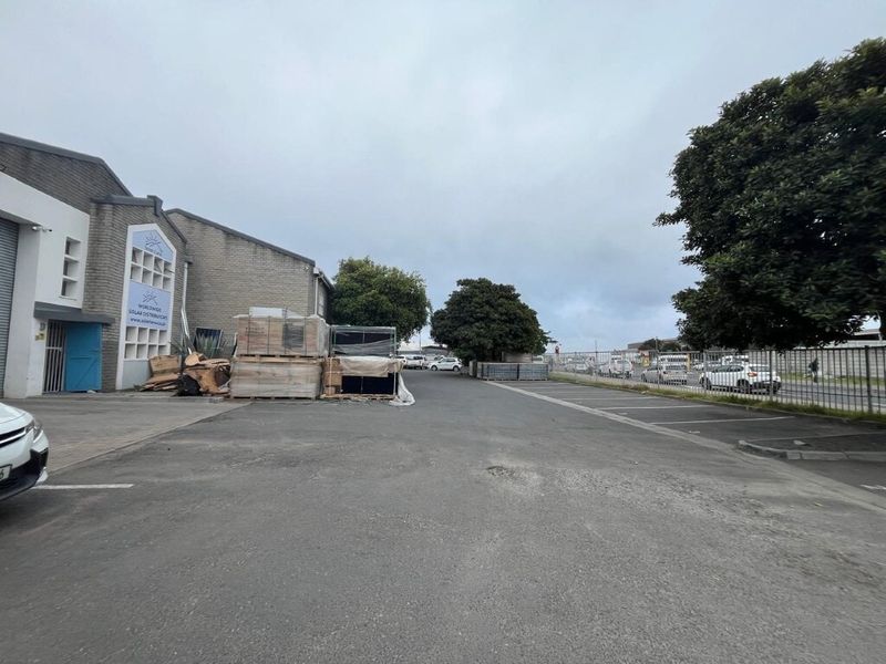 Exterior view of an industrial property featuring an asphalt driveway, security fencing, and access to the main building facade.