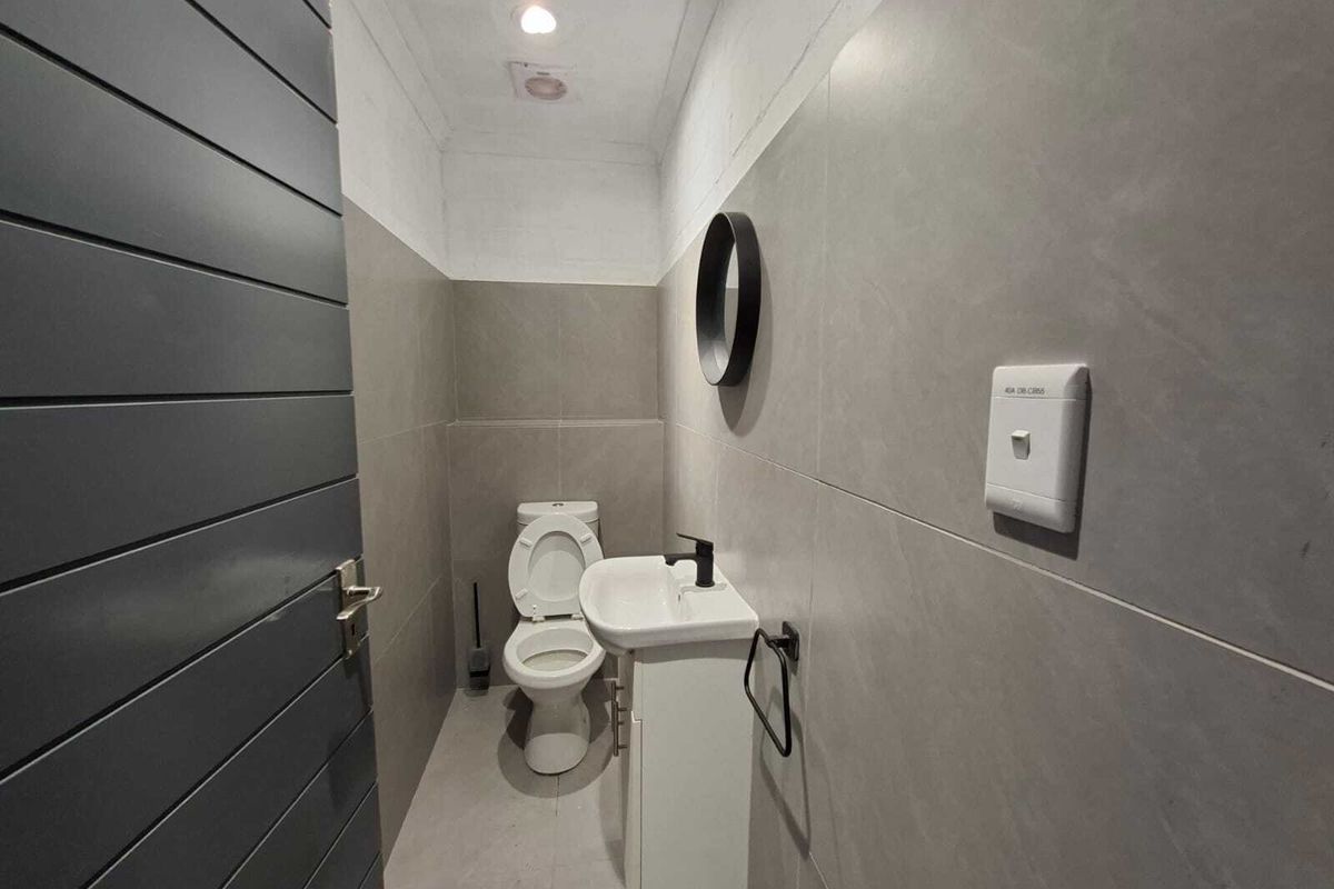 A modern, compact guest bathroom featuring large-format grey wall tiles, a sleek vanity basin, and a contemporary toilet.