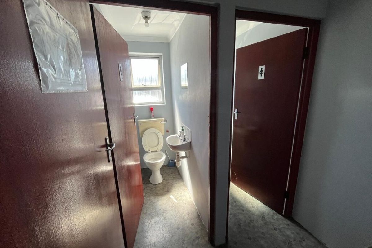 A functional industrial restroom facility featuring separate access doors, a wall-mounted basin, and a standard toilet suite.