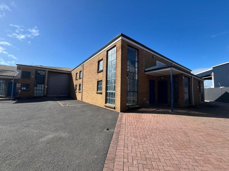 Exterior view of an industrial property featuring a brick facade, roller shutter door, paved driveway, and a covered entrance area.