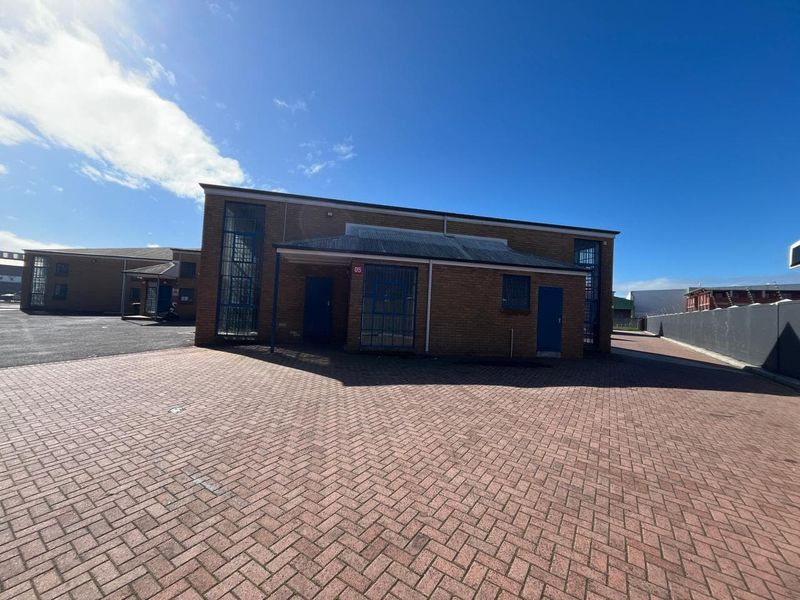 Front exterior view of an industrial unit featuring face brick construction, secure metal-framed windows, and a paved forecourt area.