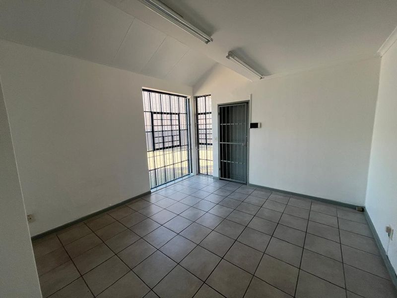A clean, empty office space featuring tiled flooring, fluorescent lighting, and secure window and door bars.
