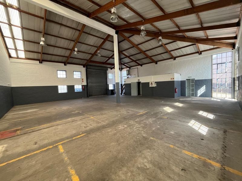 Spacious industrial warehouse unit featuring high exposed timber trusses, concrete flooring, roller shutter access, and ample natural light through translucent roof panels.
