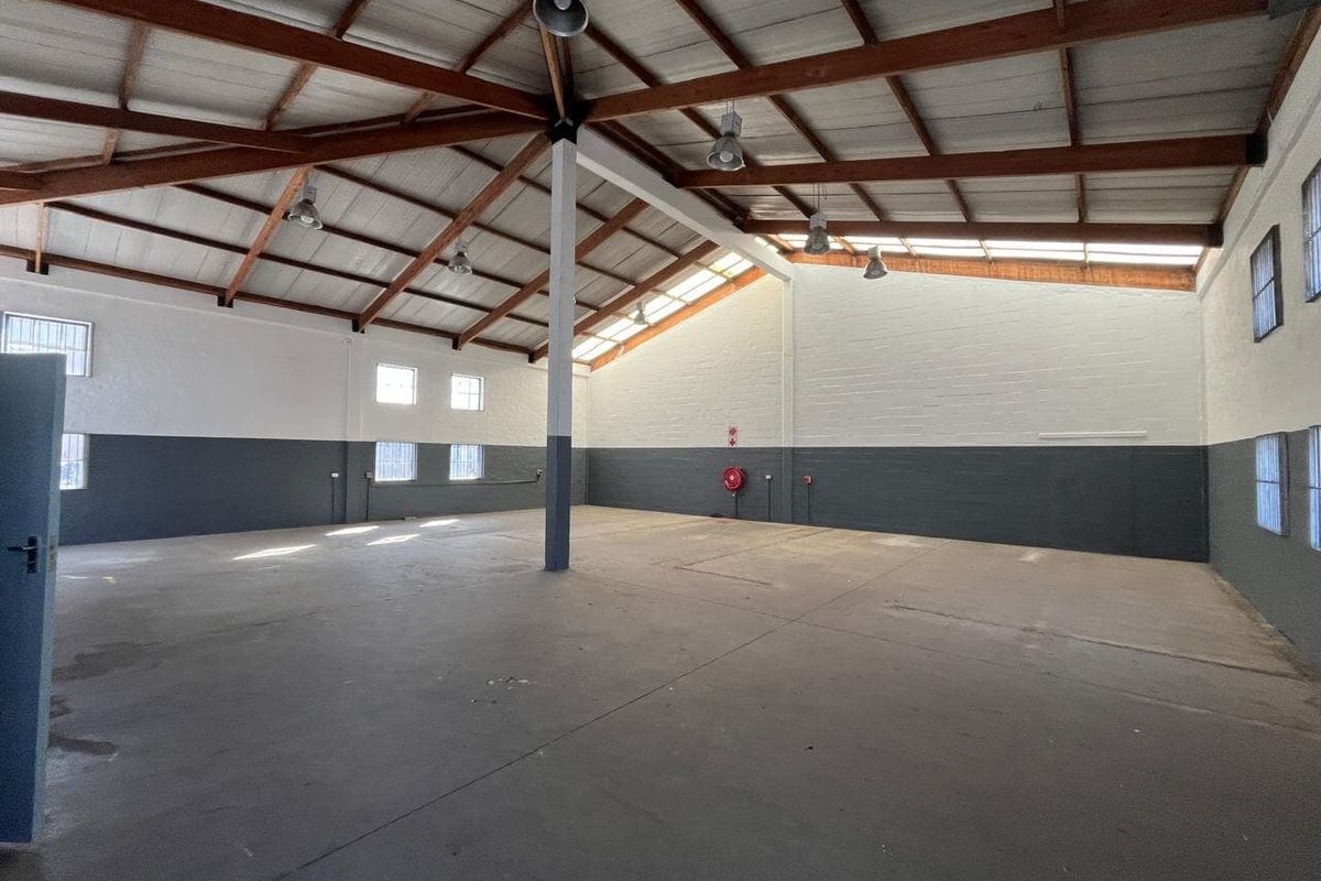 Spacious industrial utility area featuring high ceilings with exposed timber trusses, concrete flooring, and functional industrial lighting, suitable for various commercial or storage uses.