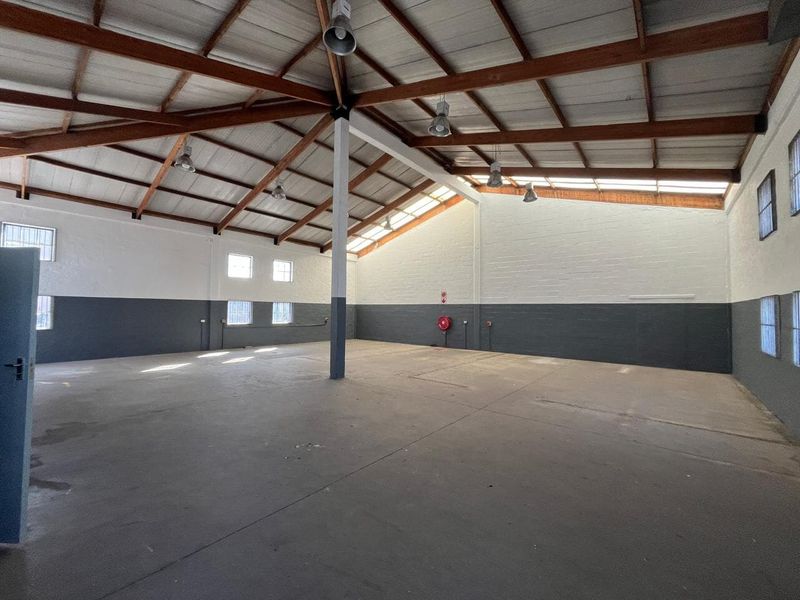 Spacious industrial utility area featuring high ceilings with exposed timber trusses, concrete flooring, and functional industrial lighting, suitable for various commercial or storage uses.