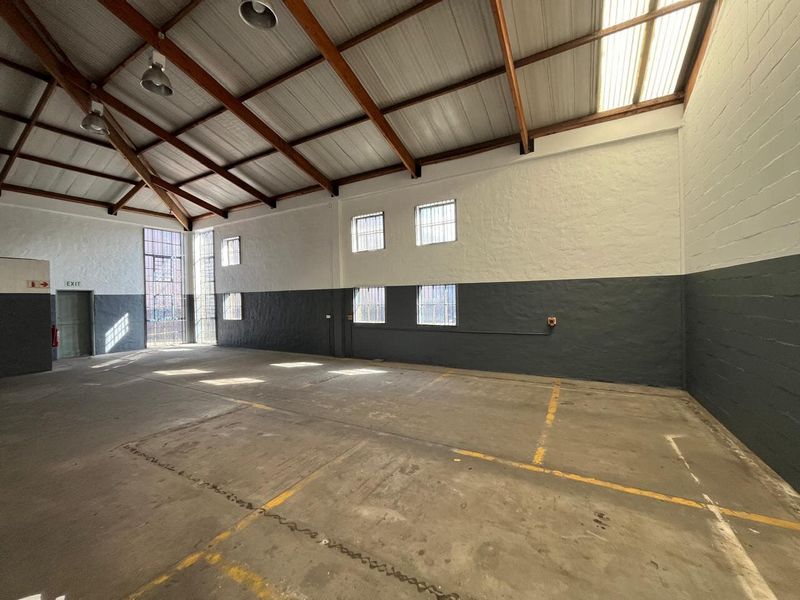 Spacious industrial utility area featuring high ceilings with exposed timber trusses, concrete flooring, and natural light from skylights and multiple windows.