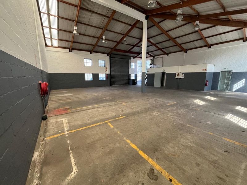 Spacious industrial warehouse unit featuring high ceilings with exposed timber trusses, concrete flooring, roller shutter access, and integrated fire safety equipment.