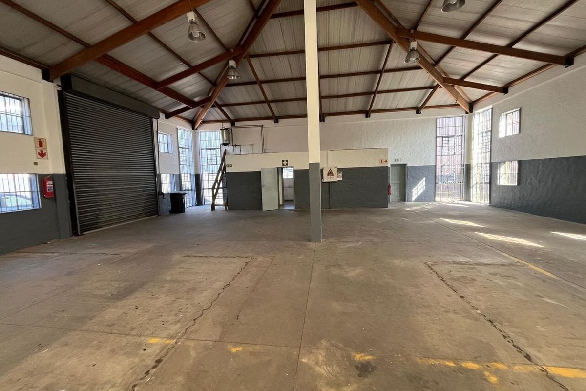 Spacious industrial warehouse featuring high exposed timber trusses, concrete flooring, large steel-framed windows, and a roller shutter door for easy access.