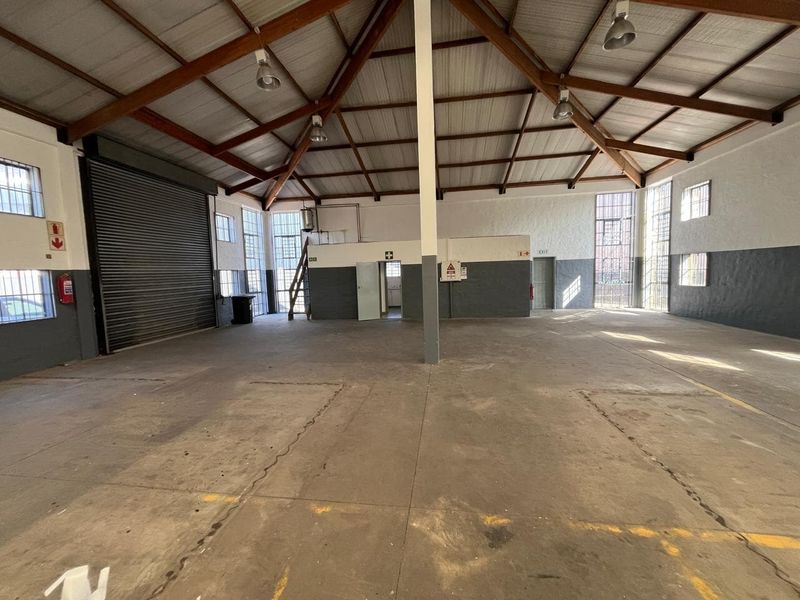 Spacious industrial warehouse featuring high exposed timber trusses, concrete flooring, large steel-framed windows, and a roller shutter door for easy access.