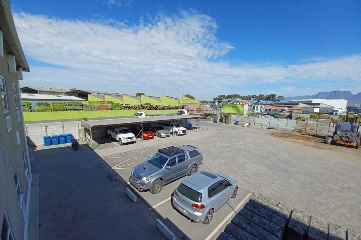 An elevated view of an industrial property featuring a paved parking area, covered parking bays, and surrounding industrial storage facilities.