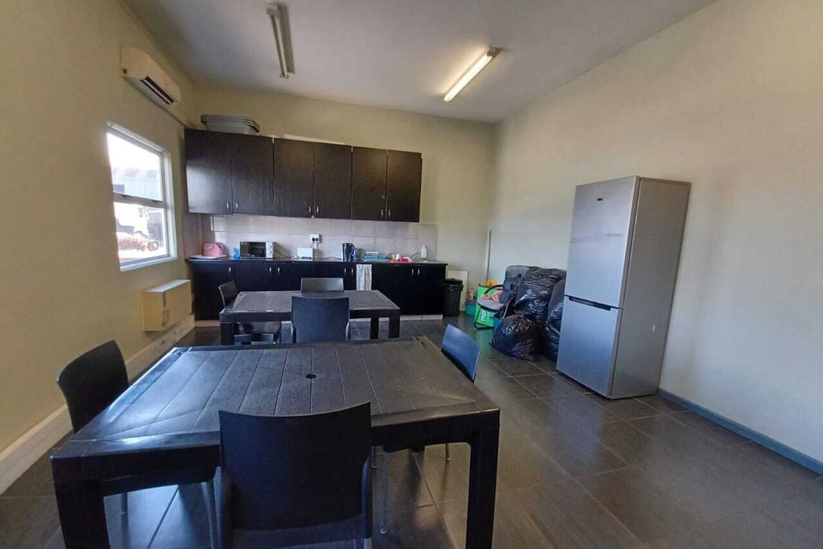 A functional industrial breakroom or kitchenette area featuring dark cabinetry, tiled flooring, and wall-mounted air conditioning unit.