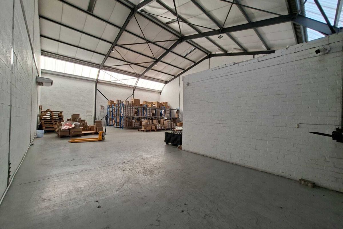 Spacious industrial warehouse unit featuring high ceilings with exposed steel trusses, painted brick walls, and durable concrete flooring with natural light from skylights.