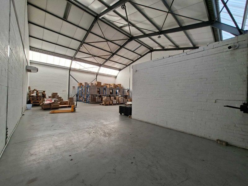 Spacious industrial warehouse unit featuring high ceilings with exposed steel trusses, painted brick walls, and durable concrete flooring with natural light from skylights.
