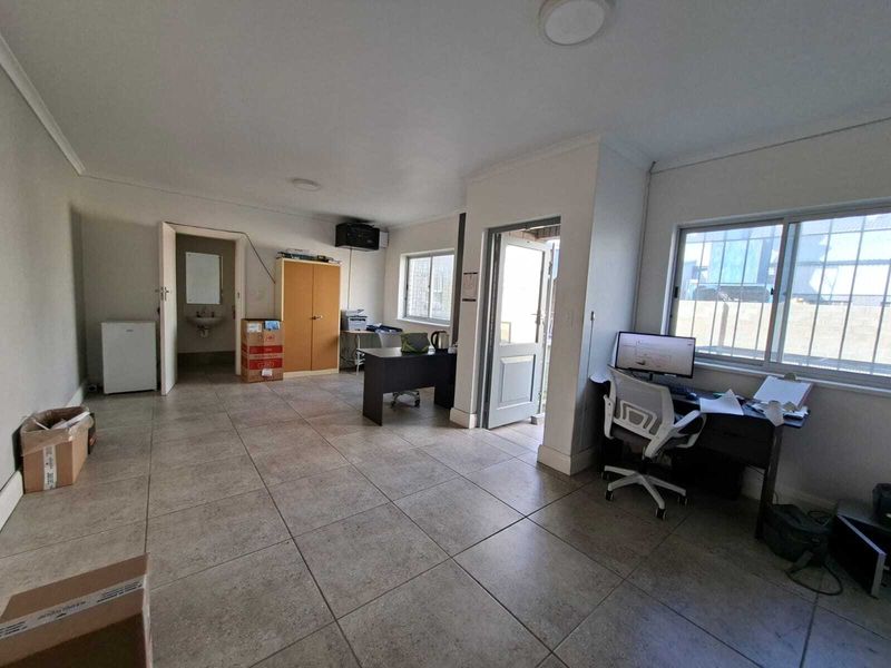 A functional office space featuring tiled flooring, large windows with security bars, and an integrated washbasin area.