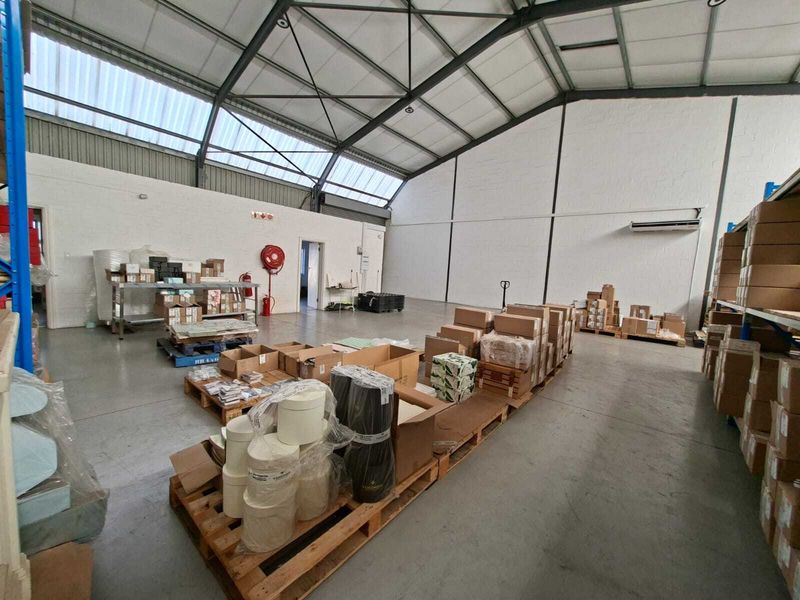 Spacious industrial warehouse unit featuring high exposed steel truss ceilings, translucent roof panels for natural light, concrete flooring, and wall-mounted climate control.