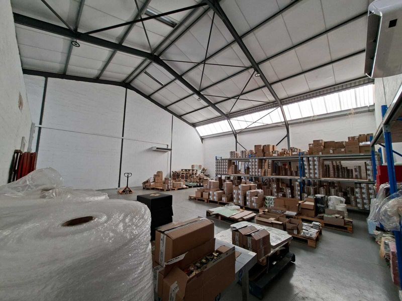 Spacious industrial warehouse featuring high ceilings with exposed steel trusses, skylights, concrete flooring, and extensive built-in racking for storage.