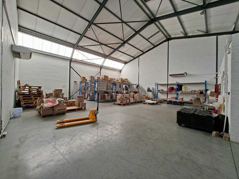 Spacious industrial warehouse featuring high ceilings with exposed steel trusses, skylights, concrete flooring, and wall-mounted HVAC units, suitable for storage or light manufacturing.