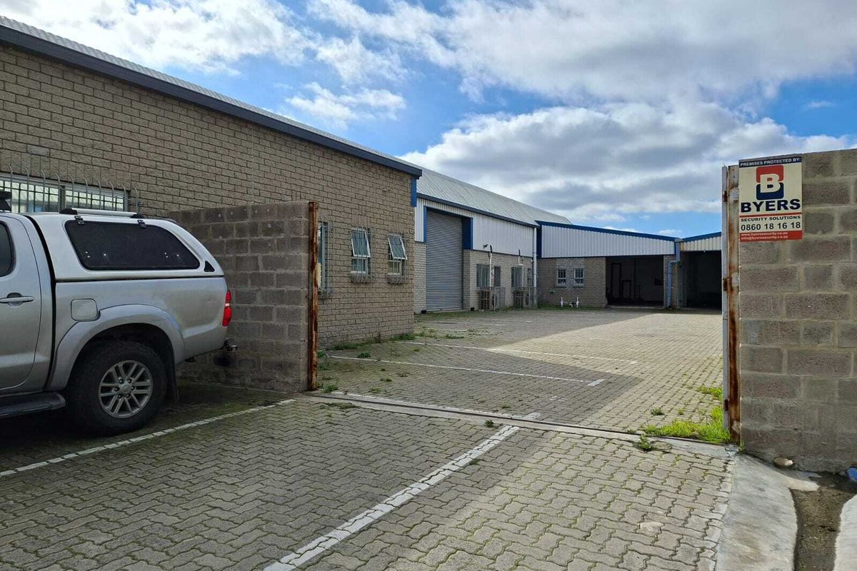Industrial property exterior featuring a paved driveway, face brick facade, and multiple roller shutter doors for access.