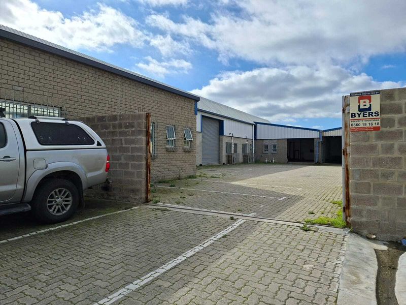 Industrial property exterior featuring a paved driveway, face brick facade, and multiple roller shutter doors for access.
