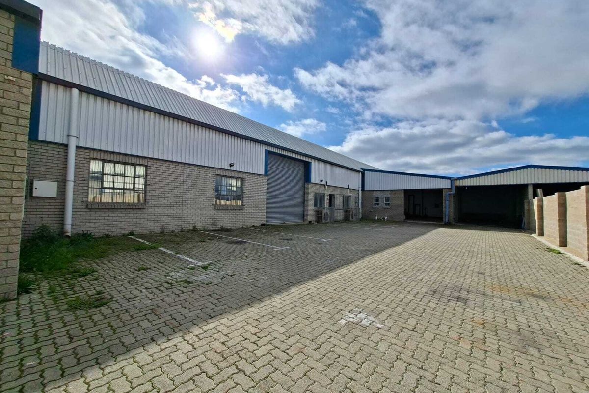 Industrial property exterior featuring a paved parking area, roller shutter access, and brick facade with metal roofing.
