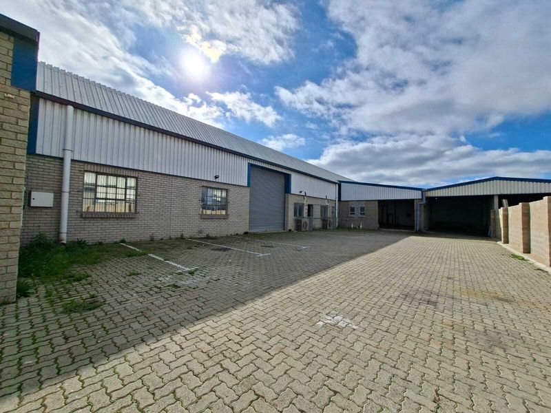 Industrial property exterior featuring a paved parking area, roller shutter access, and brick facade with metal roofing.