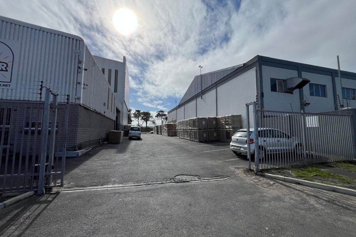 Industrial property exterior featuring a paved driveway, metal cladding structures, and secure perimeter fencing with integrated electric security measures.