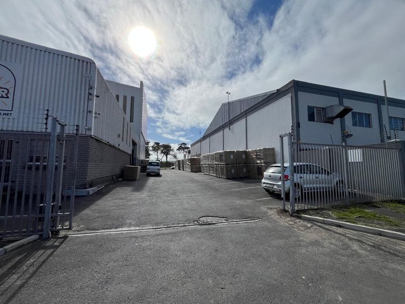 Industrial property exterior featuring a paved driveway, metal cladding structures, and secure perimeter fencing with integrated electric security measures.